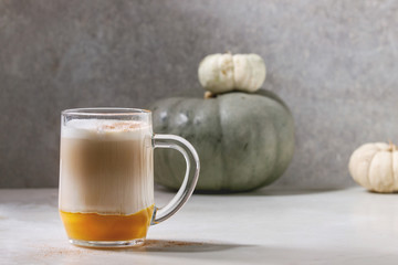 Glass of pumpkin layered spice latte with pumpkin puree, milk foam and cinnamon standing with...