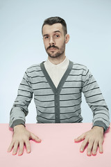 Serious business man sitting at table on blue studio background. The portrait in minimalism style