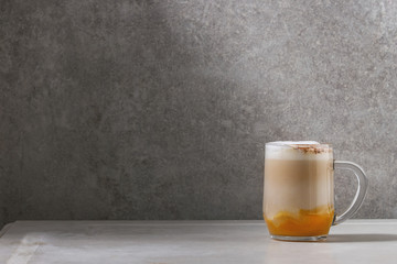Glass of pumpkin layered spice latte with pumpkin puree, milk foam and cinnamon standing on white...