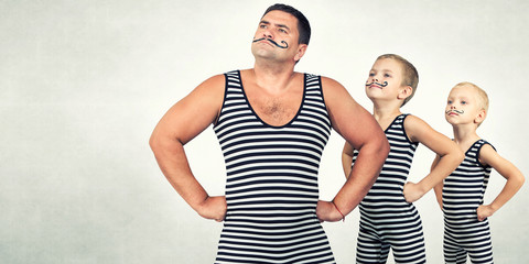  Family of strongman. The father of two sons in vintage costume of athletes perform strength exercises. Family look. © Denis