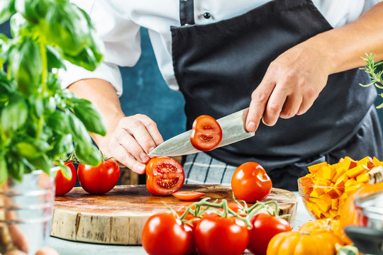 
Chef slicing fresh ripe tomatoes on a board