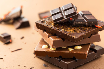 Chocolate bars with nuts, goji berries and coffee beans on a brown background