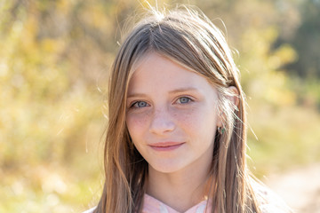 Beautiful blonde young girl with freckles outdoors on nature background in autumn, closeup portrait