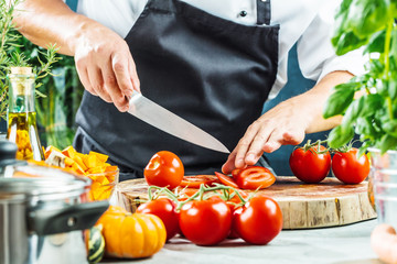 
Chef slicing fresh ripe tomatoes on a board