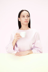 Beautiful lonely woman sitting at pink studio and looking sad holding the cup of coffee in hand. Closeup toned portrait in minimalism style