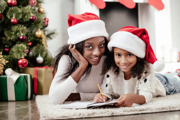 african american mother helping daughter to write letter for santa at home