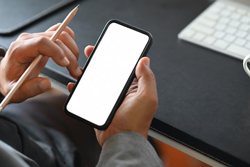 Man's hand holding white screen mobile phone on desk in office
