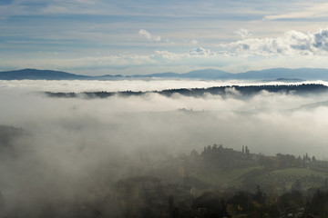 A beautiful view of the hills in Tuscany submerged by a morning mist that gives a magical touch to the scene from the top of one of the towers of San Gimignano