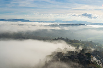 A view from an high tower in the little town of San Gimignano, tuscany italy. A sea made of fog until the horizon with light blue mountains in the background and a little town emerging from the mist 