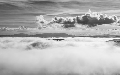 A view from an high tower in the little town of San Gimignano, tuscany italy. A sea made of fog until the horizon with light blue mountains in the background and a little town emerging from the mist 