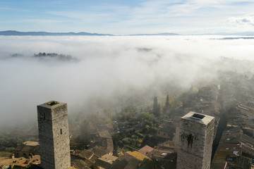 A view from an high tower in the little town of San Gimignano, tuscany italy. A sea made of fog until the horizon with light blue mountains in the background and a little town emerging from the mist 