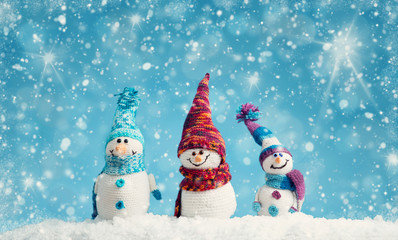 little knitted snowmans on soft snow on blue background