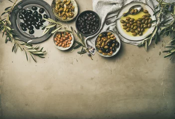 Foto op Plexiglas Plat leggen van verschillende soorten mediterrane ingemaakte olijven in borden en kommen en olijfboomtakken over grijze betonnen tafelachtergrond, bovenaanzicht, kopieerruimte. Mediterraans meze-voorgerecht © sonyakamoz