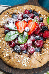 Whole-grain galette with plums and berries on dark background, top view
