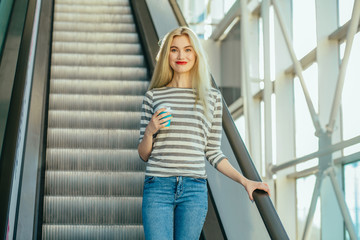 Portrait of elegant fashionable young blond woman in strip t-shirt with red lips drinking coffee to...