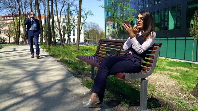 Businesswoman sitting on the bench while businessman is walks next to her, steadycam shot 
