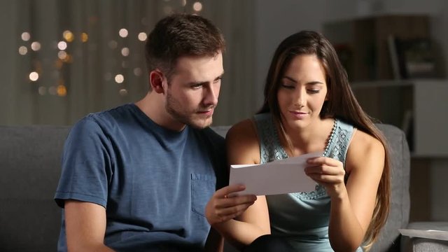 Sad couple reading bad news in a letter in the night at home