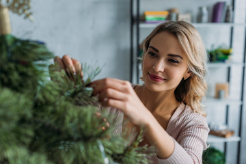 selective focus of attractive girl decorating christmas tree with baubles at home