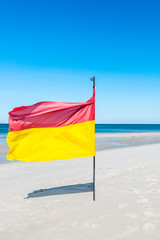 Red-yellow flag on the beach and view of the calm sea from the beach, open space, horizon.