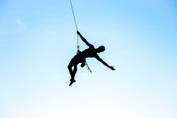View of man in hardhat hanging on rope while doing rappel and showing pirouettes flying in air © pablobenii