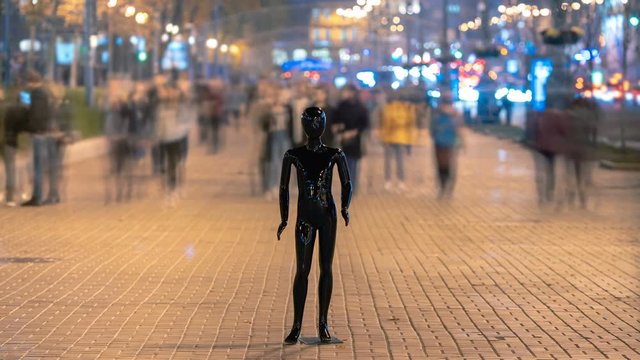 The black mannequin standing in an evening street with a people stream
