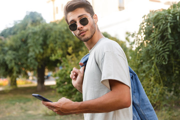 Handsome young guy walking outdoors listening music at the street using mobile phone chatting.