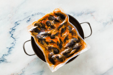 Frozen mussels in a package on a blue marble table in a skillet