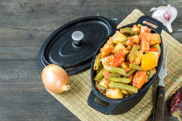   Vegetable stew. Stewed vegetables in a small cast-iron pot on an old wooden table. Vegetarian cuisine.