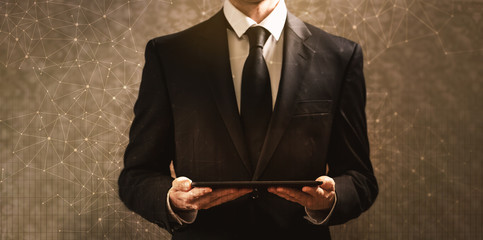 Technology links with grid with businessman holding a tablet computer on a dark vintage background