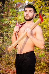 Handsome shirtless fit sexy bearded young man posing in autumn forest with an axe, lumberjack and...