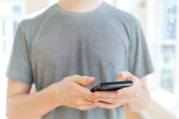 Man's hands using a smartphone on a bright interior background