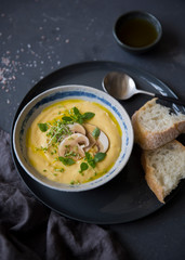 Cheese cream soup with mushrooms, herbs and white bread in gray plate on black background