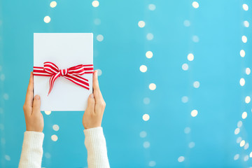 Person holding a Christmas gift box on a shiny light blue background