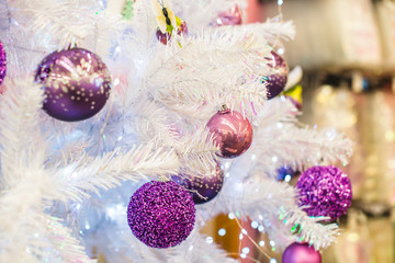 Trendy purple, ultraviolet colored baubles on silver white artificial Christmas tree. Close up. Selective focus, copy space.