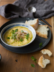 Cheese cream soup with mushrooms, herbs and white bread in gray plate on wood background