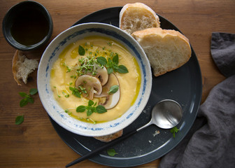 Cheese cream soup with mushrooms, herbs and white bread in gray plate on wood background