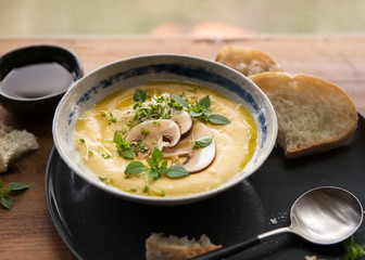 Cheese cream soup with mushrooms, herbs and white bread in gray plate on wood background