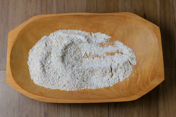 portion of raw whole wheat flour, wooden bowl, wooden table top view