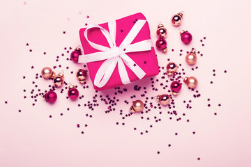 Christmas gift and balls with confetti on pink pastel background