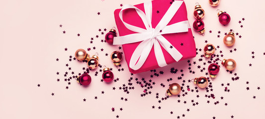 Fototapeta premium Christmas gift and balls with confetti on pastel background. Long banner format