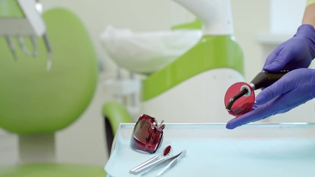 Stomatolog hands preparing polymerization lamp for oral cavity. Close up dentist hands holding dental curing light. Dental medicine equipment for tooth decay treatment in modern dental office