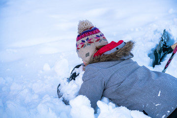 A unidentifiable young girl, embracing a pile of snow with shovel and hockey stick in background.