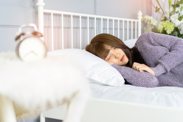 Woman stretching in bed after waking up, back view. Woman sitting near the big white window while stretching on bed after waking up with sunrise at morning, back view.