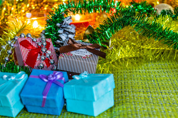 Colorful small gift boxes with gifts among Christmas tinsel and shiny toys and decorations. Winter and holiday scenery by the light of candles.