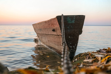 old wooden boat on a chain at the autumn shore