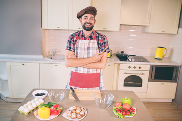 Positive man is smiling and laughing. He holds wood equipment in hand. Also guy keeps hands crossed. He is in good mood. Guy is ready to cook.