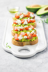 Avocado cherry tomatoes toasts on board. Selective focus, space for text.