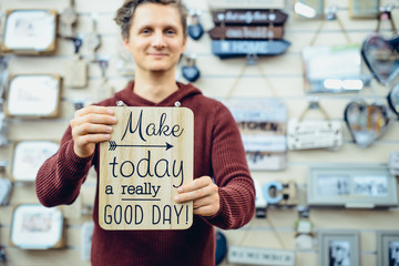 Portrait of Young smiling caucasian man holding motivational message typing on the wooden board. Everyday Inspirational quotes concept. Vintage styled toning. Selective focus.