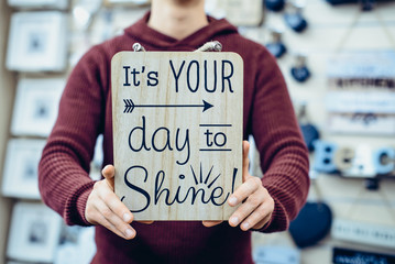 Man's hands holding motivational l's your day to shine message typing on the wooden board. Everyday Inspirational quotes concept. Vintage styled toning. Selective focus.