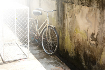 old bicycle parked near the cement wall with bright light from the sun at noon